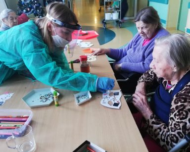 Widok z góry: psycholożka Maria Skubich-Wiczling przy stole z seniorkami przygotowują maski noworoczne