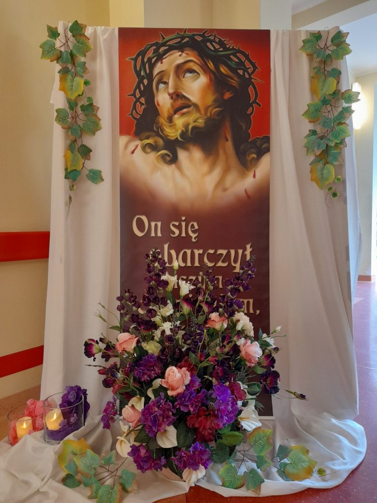 Dekoracja z fioletowymi, różowymi i białymi kwiatami z obrazem Chrystusa w koronie cierniowej
