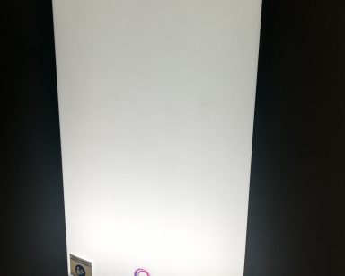 Na ciemnej ścianie wisi prostokątna lampa antydepresyjna. Lampa jest włączona. Wytwarza światło imitujące światło słoneczne