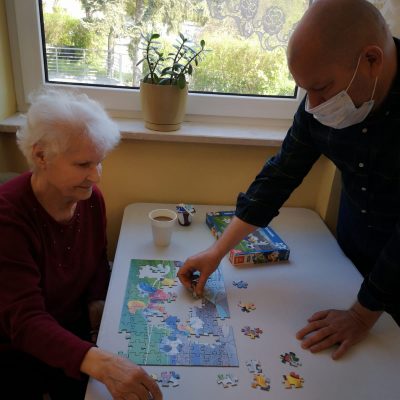 Seniorka i kierownik Arkadiusz Wanat wspólnie układają puzzle przy kawie.