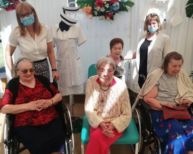 Zdjęcie grupowe pracowników i seniorów. Dekoracje: kolorowe chorągiewki, białe parawany, czepki pielęgniarskie, kwiaty.