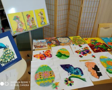 Na stoliku, stole i stelażu kolorowe obrazki. Obrazki wykonane są z bibuły, pasków kolorowego papieru, farb i kredek.