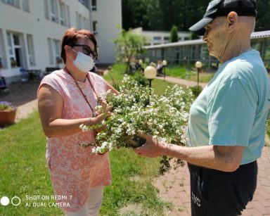 Słoneczny ogród. Koordynatorka wolontariatu Edyta Życzyńska i senior przenoszą kwiaty do zasadzenia.
