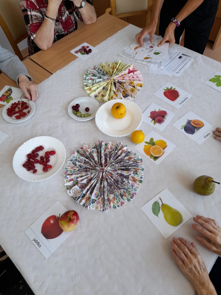 Widok z góry. Na stole obrazki i nazwy owoców, kolorowe serwetki. Na talerzach świeże owoce: maliny, porzeczki, agrest i inne.