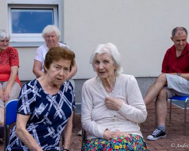 Seniorzy na patio przed budynkiem. Siedzą i rozmawiają.