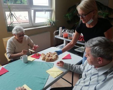 Kierowniczka Ilona Gajewska częstuje seniorów ciastem drożdżowym z rabarbarem.
