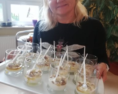 Uśmiechnięta neurologopedka Anna Szmaja-Wysocka trzyma tacę. Na tacy szklanki z jogurtowym deserem i orzechami.