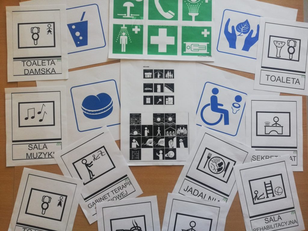 Na blacie kartki z różnymi symbolami. Pod niektórymi ilustrujące symbol napisy: toaleta, sala muzyki, gabinet terapii.