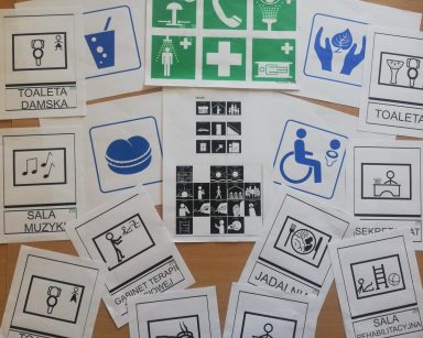 Na blacie kartki z różnymi symbolami. Pod niektórymi ilustrujące symbol napisy: toaleta, sala muzyki, gabinet terapii.