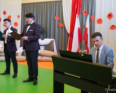 Artyści Dariusz Wójcik, Jacek Szymański, Paweł Zawada w trakcie koncertu. Za nimi dekoracja z czerwonych maków, polskie flagi.