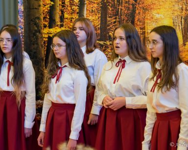 Dziewczęta z chóru ASbeek występują na sali. Jesienna dekoracja, pomarańczowe kwiaty, dynie.