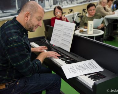 Kierownik Arkadiusz Wanat gra na pianinie. Przed nim, przy stołach seniorzy.