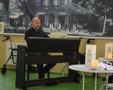 Kierownik Arkadiusz Wanat gra na pianinie. Za nim, na ścianie czarno-biały plakat przedstawiający Sopot.