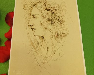 Szkic przedstawiający portret kobiety z profilu. Obok rozrzucone płatki czerwonych róż.