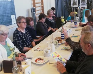 Spotkanie Związku Emerytów, Rencistów i Inwalidów. Seniorzy przy stołach, rozmawiają.