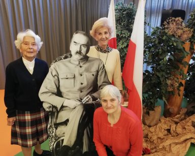 Przy tekturowej postaci Piłsudskiego trzy seniorki. Dekoracja z okazji Święta Niepodległości.