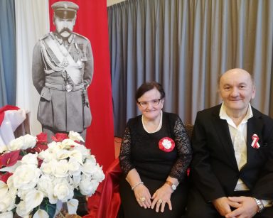 Przy tekturowej postaci Piłsudskiego siedzi dwoje seniorów. Dekoracja z okazji Święta Niepodległości.