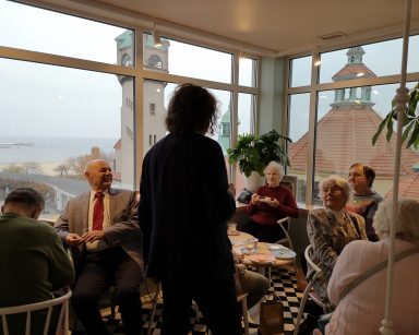 Kawiarnia. Seniorzy przy stolikach, piją kawę, jedzą ciasto, rozmawiają. Wśród nich stoi prezydent Jacek Karnowski.
