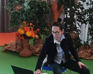 Sala. Dekoracja z zielonych roślin i kwiatów. Przy laptopie siedzi terapeutka Magdalena Poraj-Górska.