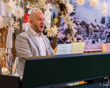 Sala. Świąteczne dekoracje, bombki, gwiazdy. Przy pianinie siedzi kierownik Arkadiusz Wanat. Gra i śpiewa.