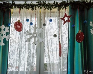 Przy oknie dekoracja. Gałązki choinki. Zawieszone bombki, gwiazdy, śnieżynki ze styropianu, ozdoby.