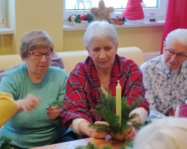 Na sali przy stole seniorzy. Robią świąteczne stroiki ze świeczek i gałązek choinki.