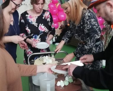 Sala. Dyrektorka Agnieszka Cysewska kroi torty. Pomagają jej pracownicy. W tle balony, napis 