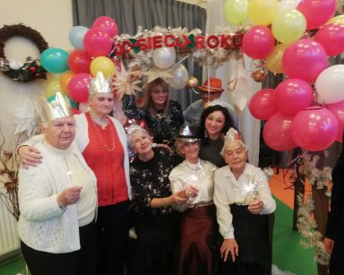 Sala. Dekoracje, balony, napis Do siego roku. Dyrektorka Agnieszka Cysewska, pracownicy, seniorzy pozują do zdjęcia.