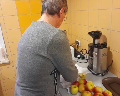 Kuchnia. Senior stoi przy blacie. Przed nim wyciskarka do soków, jabłka rozłożone na papierowym ręczniku.