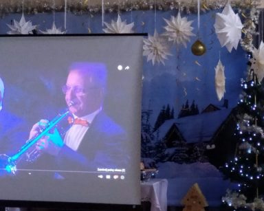 Na ekranie projektora muzycy w trakcie koncertu. Napis Koncert noworoczny - Nowy Targ 2021.