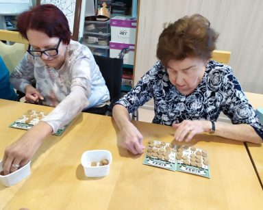 Świetlica. Seniorki siedzą przy stole. Grają w Bingo.