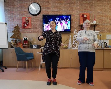 Na środku sali terapeutka Gosia Jancelewicz i seniorka. Śmieją się, pokazują figury taneczne.