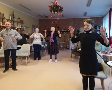 Sala. Seniorzy stoją i tańczą.