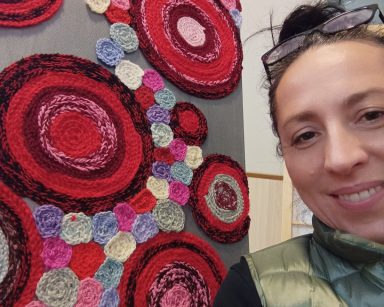 Terapeutka Magdalena Poraj-Górska uśmiecha się. Obok, na stelażu obraz z wełnianych kolorowych krążków.