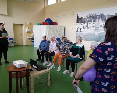 Sala gimnastyczna. Fizjoterapeutki Martyna Józefczyk, Paulina Winczura prowadzą spotkanie. Przed nimi siedzą seniorki.