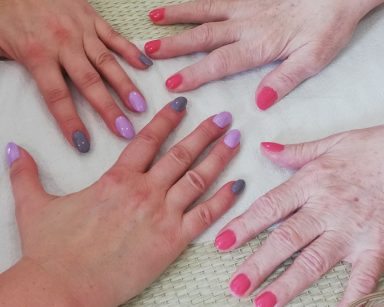 Zbliżenie na dwie pary dłoni. Prezentują paznokcie pomalowane kolorowymi lakierami.