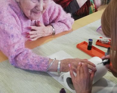 Świetlica. Dyrektorka Agnieszka Cysewska maluje paznokcie seniorce. Seniorka się śmieje.