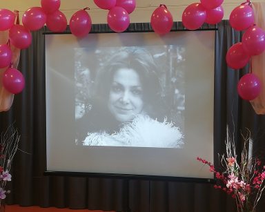 Sala. Dekoracja z różowych balonów. Ekran projektora. Na ekranie czarno-biały obraz kobiety.