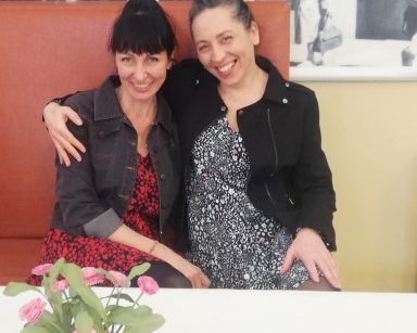 Sala. Terapeutki Ania Rzepczyńska i Magdalena Poraj-Górska siedzą przy stole. Śmieją się i obejmują.
