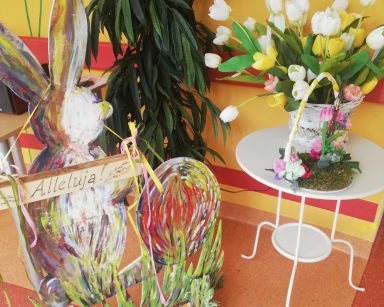 Wielkanocne dekoracje. Na stoliku kosz z bukietem tulipanów. Obok drewniany zając z napisem Alleluja!