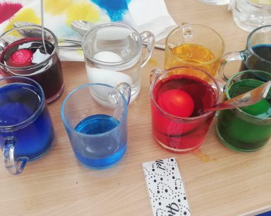 Na blacie osiem szklanek z kolorowymi barwnikami. W szklankach zanurzone jajka.