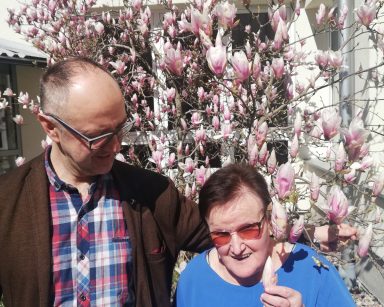 Ogród. Przy magnolii z różowymi kwiatami pozuje seniorka i Vłodimir Ivanets. Uśmiechają się.
