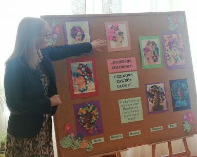 Korytarz. Dyrektorka Agnieszka Cysewska stoi przy korkowej tablicy. Na tablicy kolorowe obrazki z guzików i włóczki.