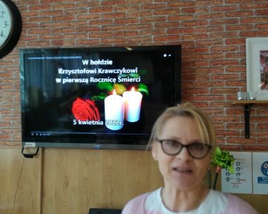 Terapeutka Beata Brzozowska przed telewizorem. Na nim tekst W hołdzie Krzysztofowi Krawczykowi w pierwszą Rocznicę Śmierci.