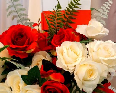 Bukiet z białych i czerwonych róż. Jest ozdobiony liśćmi paproci i flagą Polski.