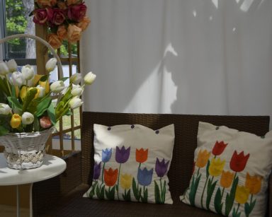 Ogród zimowy. Pergola. Na fotelu dwie poduszki wyszywane w kolorowe tulipany. Obok na stoliku wazon z kwiatami.
