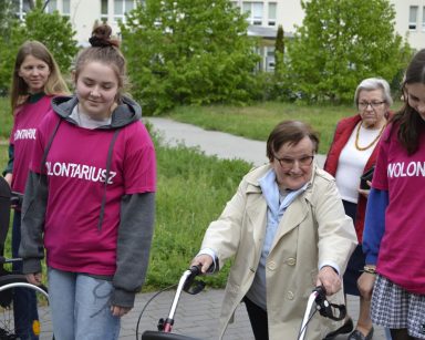 Na świeżym powietrzu spacerują wolontariusze i seniorzy. W tle budynek Domu Pomocy Społecznej w Sopocie.
