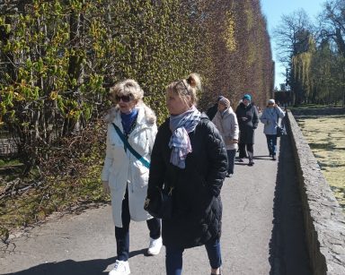 Słoneczny dzień. Terapeutka Beata Gadomska i seniorzy spacerują po Parku Oliwskim.