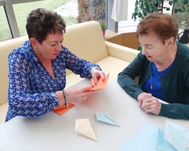 Ogród zimowy. Warsztaty origami. Kierowniczka Mariola Ludwicka i seniorka składają figury z papieru.