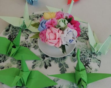 Na blacie filiżanka z bukiecikiem kwiatów. Wokół ustawione ptaki z papieru złożone techniką origami.